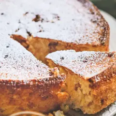 Torta di riso ricetta originale, soffice e dorata, cosparsa di zucchero a velo. Una fetta mostra la consistenza cremosa.
