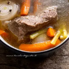 Brodo di carne ricetta: un pezzo di carne, carote, sedano e cipolla con chiodi di garofano bollono in una pentola.