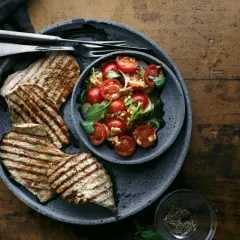 Delizioso paillard di vitello grigliato servito con un'insalata fresca di pomodorini, basilico e pinoli.