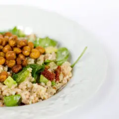 Un piatto di cous cous estivo con ceci croccanti, avocado, pomodori secchi e verdure fresche.