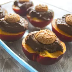 Pesche al forno con amaretti: dolci metà di pesche rosse ripiene di crema al cioccolato e guarnite con un amaretto croccante.