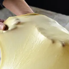 Mani che stendono la pasta matta, seguendo la ricetta originale. La pasta è sottile e traslucida, con le dita che la modellano.