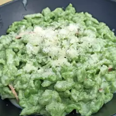 Spätzle alla tirolese verdi, conditi con panna e parmigiano, serviti in un piatto nero.