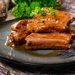 Succulente costine in umido, condite con erbe aromatiche e servite su un piatto scuro. Un piatto invitante e saporito.