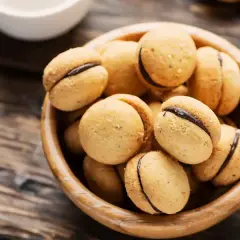 Baci di dama, deliziosi biscotti con ripieno di cioccolato, in una ciotola di legno su un tavolo rustico.