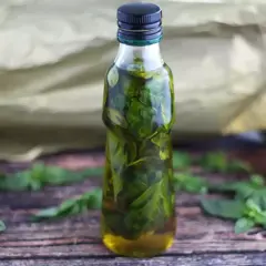Olio al basilico fatto in casa da Benedetta, profumato e verde brillante, in una bottiglia su un tavolo di legno.