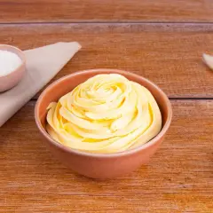 Una ciotola piena di soffice crema al burro, pronta per decorare torte. Accanto, ciotoline con zucchero e decorazioni naturali.