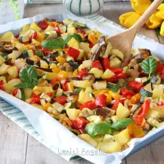 Un colorato mix di verdure in padella, con patate, peperoni, zucchine e melanzane, guarnito con basilico fresco.