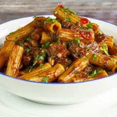 Rigatoni conditi con un saporito ragù di polpo, guarniti con prezzemolo fresco e peperoncino.
