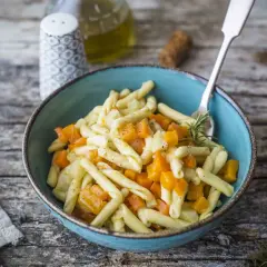 Piatto di pasta con un saporito ragù di verdure, zucca e rosmarino, servito in una ciotola blu su un tavolo di legno rustico.