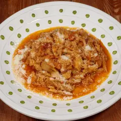 Un piatto di trippa alla fiorentina, ricca e saporita, cosparsa di parmigiano, servita su un piatto bianco decorato.