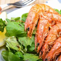 Gamberoni succulenti, pronti per la griglia, con un'insalata fresca e una fetta di limone. La marinatura per gamberoni alla griglia è il segreto del loro sapore.