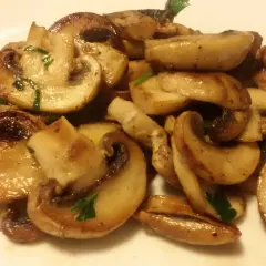 Funghi champignon in padella, dorati e succulenti, guarniti con prezzemolo fresco. Un contorno semplice e gustoso.