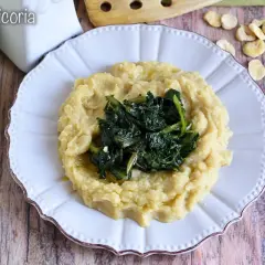 Piatto di fave e cicoria, un classico della cucina pugliese, servito su un piatto bianco con fave secche sparse attorno.