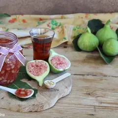 Un vasetto di marmellata di fichi, con fichi freschi, un bicchierino di liquore e un cucchiaino con la marmellata.