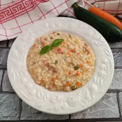 Un cremoso risotto con verdure, guarnito con basilico fresco. Accanto, carote, zucchine e cipolla, ingredienti per un piatto gustoso.