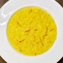 Un cremoso risotto alla milanese, giallo intenso con fili di zafferano, servito in un piatto bianco.