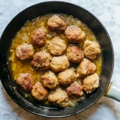Polpette in bianco cremose in padella, dorate e succulente, pronte per essere gustate con un cucchiaio di legno.