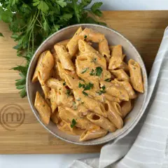 Penne alla vodka cremose e invitanti, guarnite con prezzemolo fresco, su un tagliere di legno con il logo MasterChef.