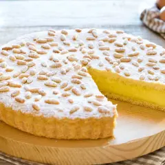 Una deliziosa torta della nonna, con crema gialla e pinoli tostati, spolverata di zucchero a velo.