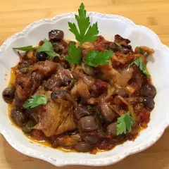 Un piatto invitante di melanzane in agrodolce, con olive nere e capperi, guarnito con prezzemolo fresco.