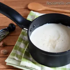 Besciamella senza glutine cremosa in pentolino, con noce moscata grattugiata. Accanto, noce moscata intera e una grattugia.