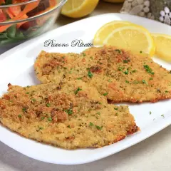 Due cotolette di pollo al forno dorate e croccanti, guarnite con prezzemolo fresco e servite con spicchi di limone e un'insalata mista.