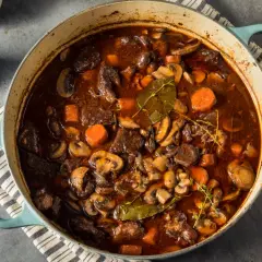 Un invitante spezzatino con funghi, carote e erbe aromatiche in una casseruola blu.