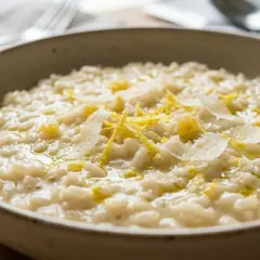 Cremoso risotto al limone, guarnito con scorza di limone e scaglie di parmigiano, pronto per essere gustato.