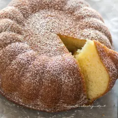 Torta 7 vasetti soffice e dorata, cosparsa di zucchero a velo. Una fetta è stata tagliata, rivelando l'interno profumato.
