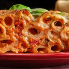 Un primo piatto invitante di ziti al forno, con sugo rosso e formaggio filante, guarnito con foglie di basilico fresco.
