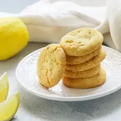 Biscotti senza burro al limone, dorati e fragranti, su un piatto bianco, con limoni freschi a lato.
