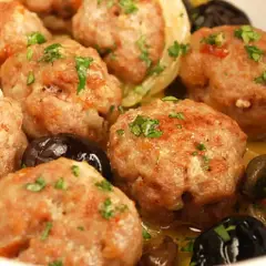 Polpette di carne succulente, dorate e profumate, servite con olive nere e un contorno di verdure.