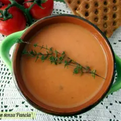 Una ciotola di cremosa crema di pomodoro, guarnita con timo fresco, accanto a pomodori maturi e cracker croccanti.