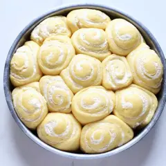 Torta di rose lievitata, pronta per essere infornata, con soffici spirali di pasta e una spolverata di zucchero a velo.