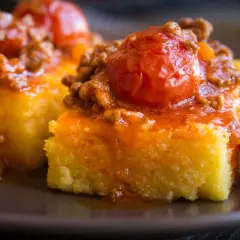 Polenta morbida ricoperta da un ricco sugo con salsiccia e pomodorini. Un piatto confortante e saporito.