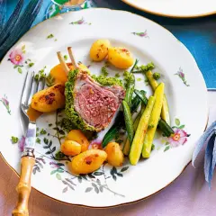 Carrè di agnello croccante con patate novelle e zucchine, un piatto elegante su un piatto fiorito.