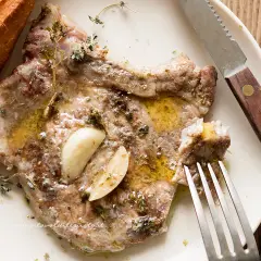 Succulenta braciola di maiale condita con aglio e erbe aromatiche, servita con pane croccante.