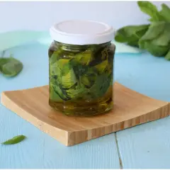 Un barattolo di olio al basilico fatto in casa, con foglie fresche immerse nell'olio dorato, su un tagliere di legno.