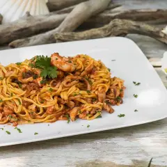 Un piatto di linguine al ragù di pesce, con gamberi e calamari, guarnito con prezzemolo e spicchi di limone su una conchiglia.