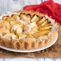 Una crostata di mele semplicissima, con mele a fette disposte a raggiera sulla base dorata, spolverata di zucchero a velo.