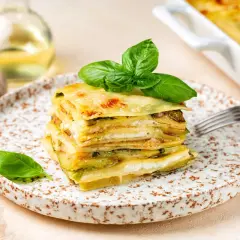 Una fetta di parmigiana di zucchine bianca alla napoletana, stratificata e dorata, guarnita con basilico fresco.