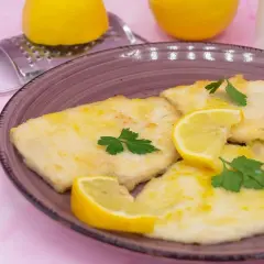 Deliziose scaloppine al limone, dorate e profumate, guarnite con spicchi di limone fresco e prezzemolo.
