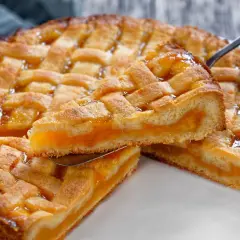 Deliziosa crostata senza glutine con ripieno di albicocche, la fetta sollevata mostra la morbidezza dell'impasto e la succosità della frutta.