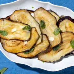 Fette di melanzane grigliate, guarnite con menta fresca e aglio, un contorno di verdure saporito e colorato.