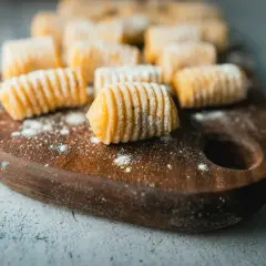 Gnocchi fatti in casa, pronti per la cottura. La **gnocchi ricetta perfetta** è a portata di mano su un tagliere di legno.