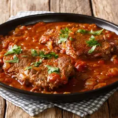 Carne alla pizzaiola morbida, succulenta e profumata, servita in un piatto scuro su un tavolo di legno.