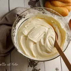 Una ciotola di soffice crema al mascarpone, pronta per preparare un delizioso tiramisù. Accanto, savoiardi e gusci d'uovo.