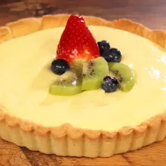 Deliziosa crostata con crema pasticcera, guarnita con fragola, kiwi e mirtilli. Un dolce invitante su un tavolo di legno.
