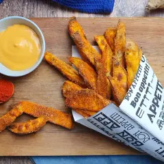 Patate dolci fritte croccanti, servite in un cono di carta con la scritta "Bon appétit!", accompagnate da una salsa cremosa e paprika.